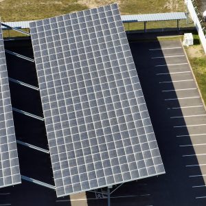 Aerial view of solar panels installed over parking lot with parked cars for effective generation of clean energy.