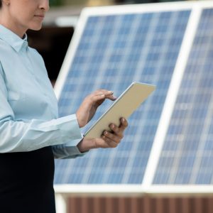 Businesswoman working on tablet computer when standing against photovoltaic panels on solar power station